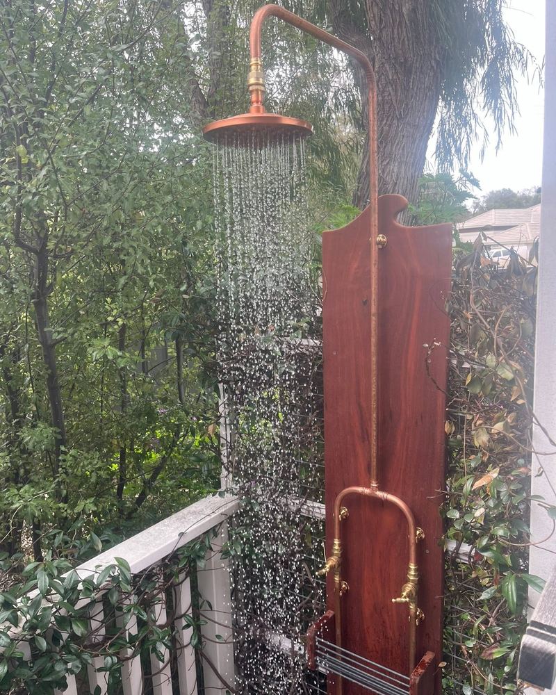 Copper outdoor shower on a jarrah board, running, with a soap rack