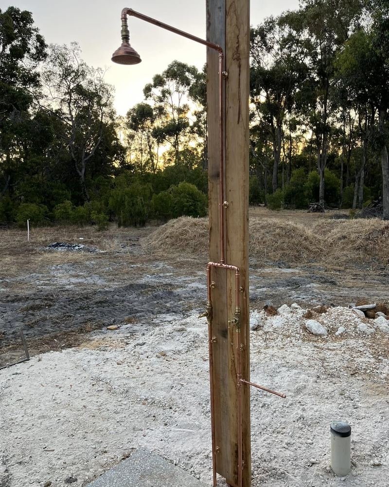 Copper outdoor shower on a timber post on a rural block at dusk