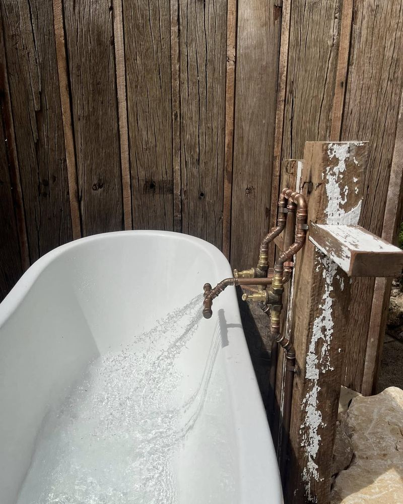 Outdoor bath filling from a copper tap on a timber post